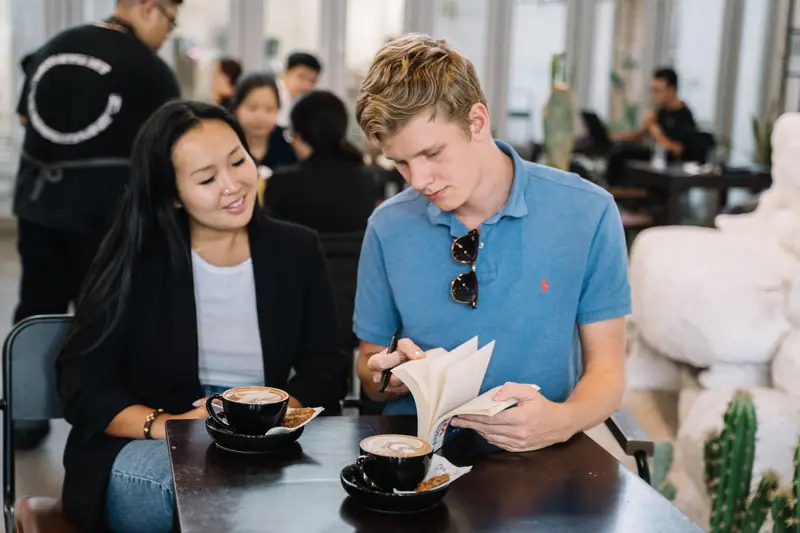 To voksne venner som snakker sammen over kaffe og en bok på en kafé