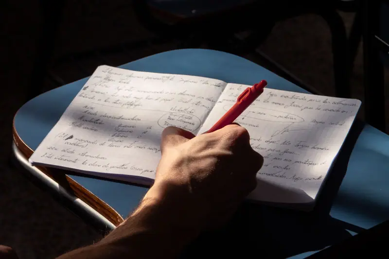 Hånd som skriver notater med penn ved en bærbar PC i dagslys